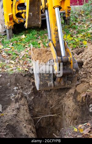 Der Bagger gräbt ein Loch. Ein gelber Pfeil mit einem Eimer schaufelt die Erde heraus und bereitet einen Graben für einen Kanalbrunnen vor. Stockfoto