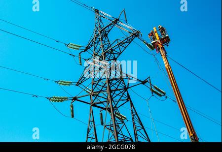 Hochspannungs-Hochspannungsleitung, Turmarbeiter mit Kran und blauem Himmel. Hydro-Linemen an Auslegerliften, die an Hochspannungstürmen arbeiten. Stockfoto