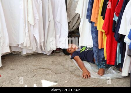 Beirut, Libanon. August 2021. Ein Kind schläft am 8. August 2021 am Kleiderstand seines Vaters im Souq el Ahad (Sonntagsmarkt), Beirut, Libanon. Die Preiserhöhung ist für den Libanon zu einem harten Problem geworden, da mehr als die Hälfte der Bevölkerung seit Beginn der Wirtschafts- und Finanzkrise im Jahr 2019 unter die Armutsgrenze gefallen ist. Die Mittelschicht ist weggewischt worden und immer weniger Menschen können es sich leisten, in den Geschäften Schuhe und Kleidungsstücke zu kaufen.(Foto: Elisa Gestri/Sipa USA) Quelle: SIPA USA/Alamy Live News Stockfoto