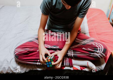 Lateinischer Teenager, der einen Rubik's Cube löst, während er in Lateinamerika auf dem Bett sitzt Stockfoto