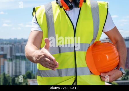 Der Baumeister hält eine Hand für einen Handschlag und die andere einen orangen Helm Stockfoto