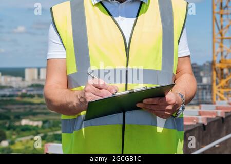 Hände eines reifen Mannes auf der Baustelle schreiben Notizen auf die Zwischenablage Nahaufnahme Stockfoto