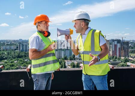 Wütender Chef brüllt im Megaphon vor seinem Baumeister auf der Baustelle Stockfoto