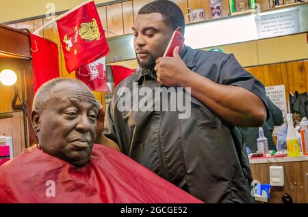 Ein Barbier spricht am Telefon, während er in Gibsons Hair Styles and Cuts am 23. April 2013 in West Point, Mississippi, Haare schneidet. Die Einheimischen sagen, dass Arbeitsplätze gebraucht werden Stockfoto