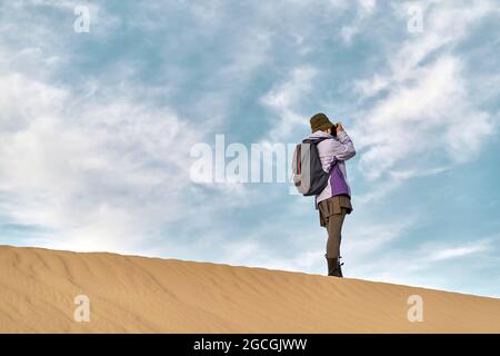 asiatische Fotografin, die auf einer Sanddüne steht und ein Bild fotografiert Stockfoto