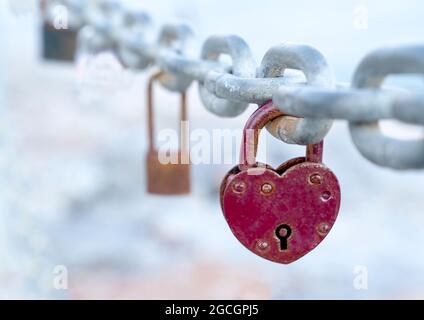 An der Brückenkette hängt ein rotes herzförmiges Schloss. Die Hochzeit Brauch ist ein Symbol der ewigen Liebe. Nahaufnahme. Stockfoto