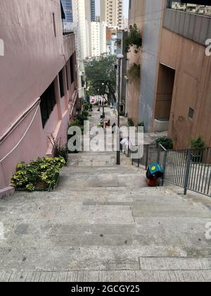 Riesige lange Treppen in Sheung Wan, die einen Berg hinunter in das Herz der riesigen Stadt führen. Pflanzen und Abfalleimer säumen die Seiten. Stockfoto
