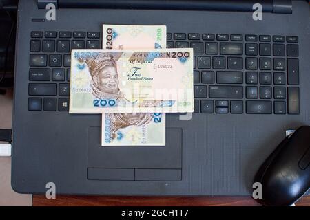 Mehrere Naira-Geldscheine, Bargeld oder nigrische Währung werden ordentlich auf dem Schlüsselbrett eines Laptops verteilt Stockfoto