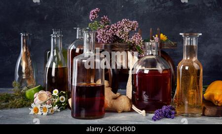 Verschiedene Glasflaschen mit alternativer Medizin aus Kräutern und Blumen auf dunklem Hintergrund. Stockfoto