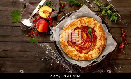 Pfirsich-Gallete auf Backpapier auf Holzhintergrund. Frisch zubereiteter hausgemachter Kuchen. Draufsicht, flach liegend, Kopierbereich Stockfoto