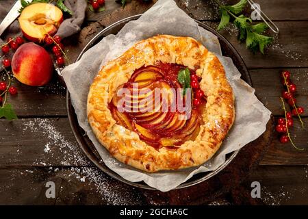 Pfirsich-Gallete auf Backpapier auf Holzhintergrund. Frisch zubereiteter hausgemachter Kuchen. Draufsicht, flach liegend Stockfoto