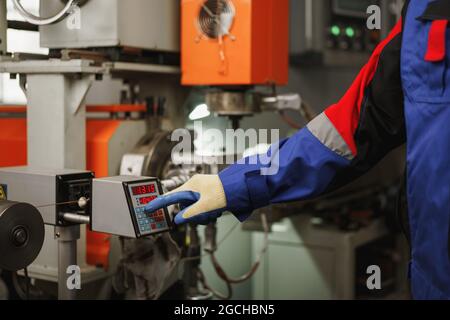 Arbeiter, der eine Maschine in einem Werk betätigt, indem er einen Knopf drückt Stockfoto