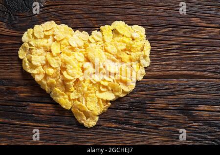 Maisflocken in Herzform auf dunklem Holztisch, Draufsicht mit Kopierraum Stockfoto