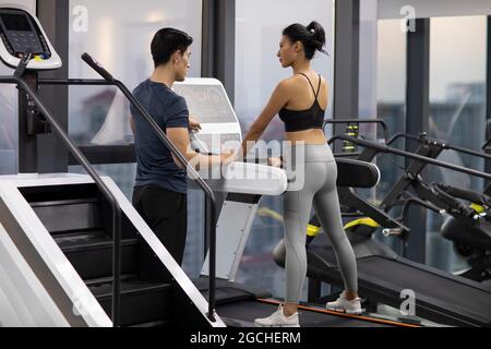Junge Frau, die im Fitnessstudio mit Personal Trainer trainiert Stockfoto