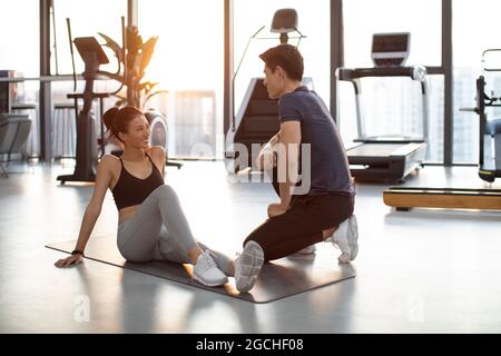 Junge Frau, die im Fitnessstudio mit Personal Trainer spricht Stockfoto