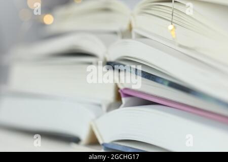 Lesen von Büchern. Bücher mit weißen Einbänden stapeln Nahaufnahme und Girlande auf verschwommenem blauem Hintergrund.Literatur- und Hobbykonzept. Stockfoto