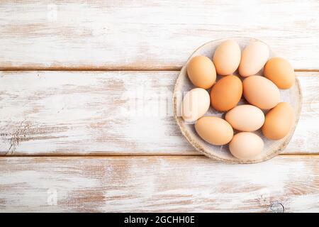 Stapel von bunten Hühnereiern auf dem Teller auf weißem Holzhintergrund. Draufsicht, flach liegend, Kopierraum. Stockfoto