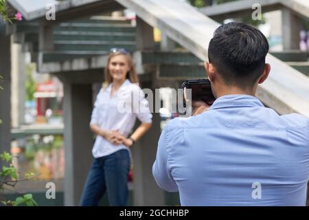 Junger Mann mit Digitalkamera, der Fotos von einer ziemlich lächelnden Freundin fotografiert, wenn sie in der Stadt spazieren Stockfoto