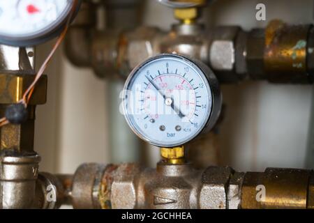 Komplexes Rohrleitungssystem mit heißem analogem Manometer mit Staub, Schmutz, schmutzigen Flecken. Wasserverteiler mit Manometer und Druckregelventil. Stockfoto