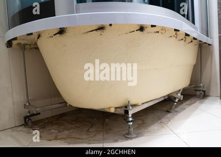 Schmutzige Pfütze, Schmutz, Haare, Staub, Schimmel, Bakterien, Pilze auf dem Boden unter dem Badezimmer. Innenseite der Acrylbadewanne ohne Zierpaneel. Rostig Stockfoto