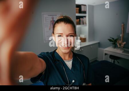 Kaukasische Ärztin, die Selfie in der Arztpraxis mit zellulärem Gerät nimmt Stockfoto