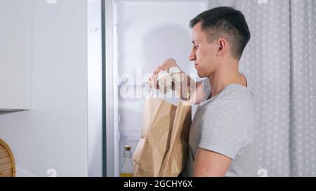 Der junge Mann stellt verschiedene Lebensmittel in einen großen Kühlschrank Stockfoto
