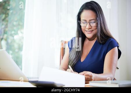 Lächelnde, elegante Geschäftsfrau, die am Schreibtisch Bericht unterschreibt und einen Vertrag unterzeichnet Stockfoto