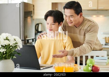 Lächelnder Vater klopfend Teenager-Sohn auf der Schulter, wenn sie die Schule Textpunktzahlen überprüfen Stockfoto