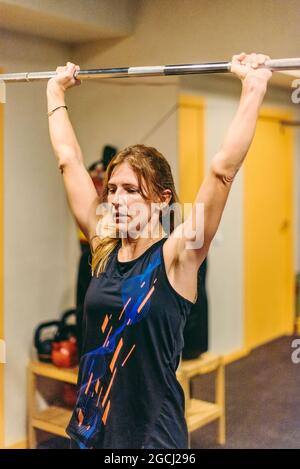 Athletin Frau macht Presseübungen mit Bar im Fitnessstudio Stockfoto