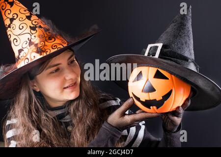 Eine Frau in einem Hexenkostüm in einem orangefarbenen Hut hält einen Kürbis-Laterne-Jack. Menschen Halloween. Stockfoto