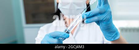 Ein Arzt mit Handschuhen zieht ein Medikament aus einer Ampulle in eine Spritze Stockfoto