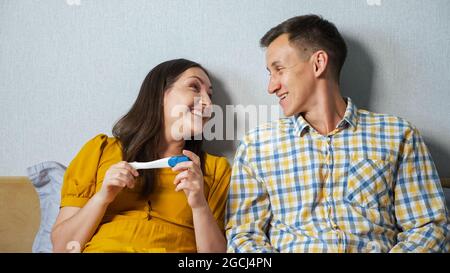 Mann und Frau beobachten eifrig das Ergebnis des Schwangerschaftstests, während sie im Bett sitzen Stockfoto
