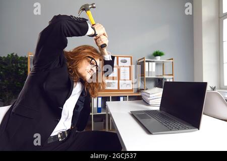 Wütend gestresste Büroangestellte schlagen Laptop-Computer mit Hammer an schlechten Tag bei der Arbeit Stockfoto