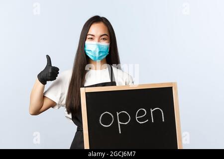 Kleinunternehmen, covid-19 Pandemie, Prävention von Viren und Mitarbeiter Konzept. Lächelnd nette asiatische weibliche Angestellte, Café oder Geschäft Arbeiter mit offenem Schild Stockfoto