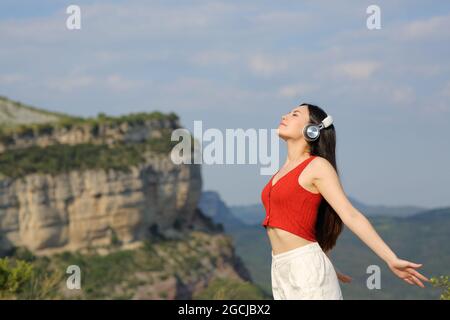 Entspannte asiatische Frau trägt Kopfhörer meditieren hören Audio-Guide im Freien in den Bergen Stockfoto