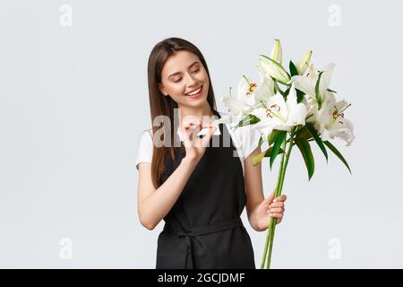 Shopping, Mitarbeiter und Kleinunternehmen Konzept. Lächelnd niedlichen Blumengeschäft Besitzer in schwarz Schürze laufen Geschäft, bereiten schöne Bouquet von weißen Lilien Stockfoto