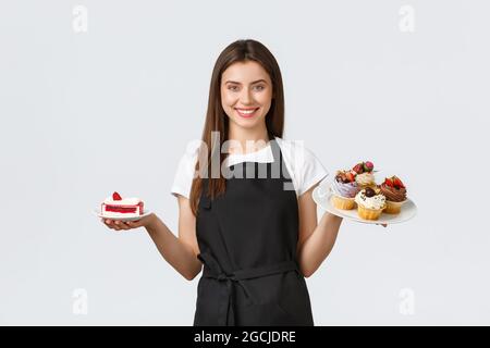 Lebensmittelgeschäft Mitarbeiter, kleine Unternehmen und Cafés Konzept. Freundliche lächelnde Kellnerin im Cafe hält Teller mit Cupcakes und Cafe, serviert Stockfoto