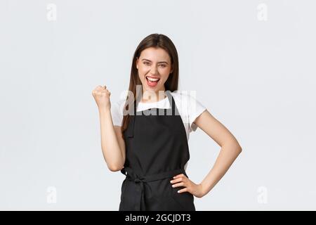 Lebensmittelgeschäft Mitarbeiter, kleine Unternehmen und Cafés Konzept. Glückliche weibliche Barista in schwarzer Schürze Faust Pumpe in freuen, feiern groß Stockfoto