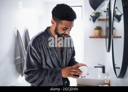 Junger Mann, der zuhause, morgens oder abends Gesichtscreme auf das Gesicht aufgibt. Stockfoto