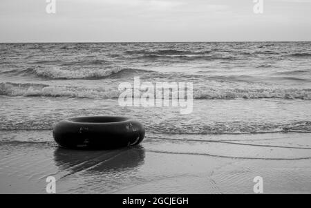 Einfarbiger schwarzer Schwimmring am Strand in Schwarz-Weiß-Tönen. Gummiring schwimmt im Meer mit Kopierraum. Stockfoto