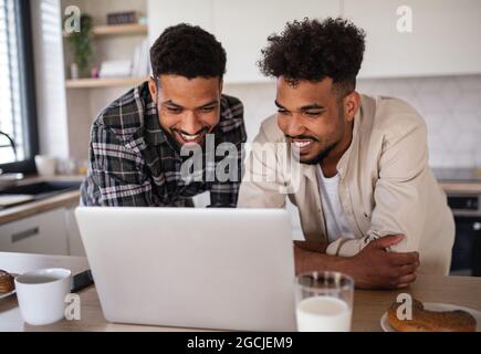 Junge Studentenbrüder, die zuhause in der Küche mit einem Laptop arbeiten. Stockfoto