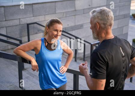 Die wunderschöne Sportlerin lächelt, während sie mit ihrem Mann oder Freund spricht und nach dem Training in der Stadt draußen steht Stockfoto