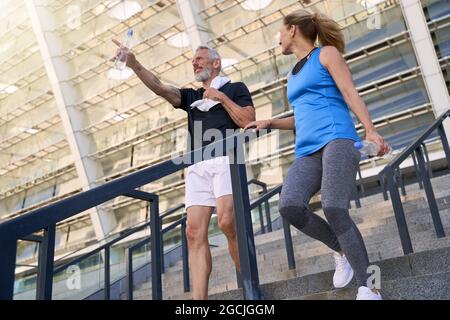 Blick aus der unteren Perspektive auf ein reifes Paar, einen Mann und eine Frau in Sportkleidung, die nach dem gemeinsamen Sport im Freien die Treppe hinuntergehen Stockfoto