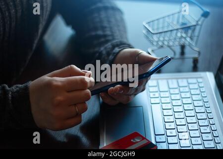 Halten eines Smartphones im Hintergrund eines Laptops und einer Bankkarte. Online-Zahlungskonzept Stockfoto