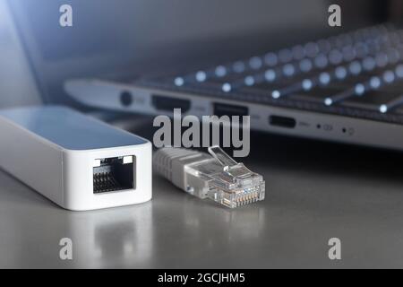 Adapter zum Anschließen eines Internetkabels an einen Laptop und eines Internetkabels mit RJ-45-Anschluss in Nahaufnahme auf einem Laptop-Hintergrund Stockfoto