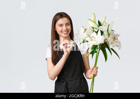 Shopping, Mitarbeiter und Kleinunternehmen Konzept. Lächelnd hübsche Verkäuferin Floristin im Blumenladen hält Bouquet von weißen Lilien und lächelnd, bereiten Stockfoto