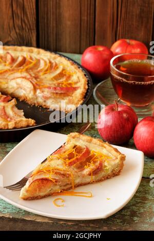 Hausgemachte Apfeltorte mit Sauerrahm mit schwarzem Tee und ganzen frischen Äpfeln vertikal Stockfoto