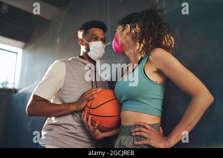 Mann und Frau, die mit Basketball befreundet sind, trainieren im Freien in der Stadt und sprechen. Coronavirus-Konzept. Stockfoto