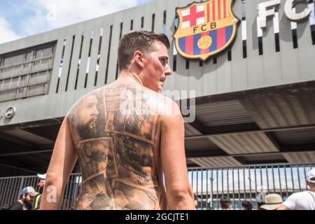 Barcelona, Katalonien, Spanien. August 2021. Lionel Messi Fan mit einem Tattoo auf dem Rücken mit dem Gesicht von Messi und anderen Idolen des FC Barcelona, wie Ronaldinho (Ronaldo de Assis) Und Andres Iniesta ist am Tor des Camp Nou Stadions zu sehen.Lionel Messi Fan mit einem FC Barcelona Messi 10 Shirt ist am Tor des Camp Nou Stadions zu sehen.Lionel Messi Fans werden mit dem FC Barcelona Messi 10 Shirt am Tor des Camp Nou Stadions gesehen.zur Zeit der Presse Abschiedskonferenz von Lionel Messi vom FC Barcelona, Fans des Spielers waren vor der Tür des Stadions von Camp Nou, um zu versuchen, Auf Wiedersehen zu sagen Stockfoto