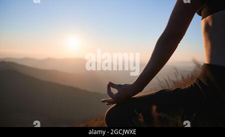 Nahaufnahme der weiblichen Hand in Gyan Mudra-Position mit schönem Abendhimmel im Hintergrund. Junge Frau macht Yoga-Übungen und meditiert während des Sonnenuntergangs in den Bergen. Stockfoto